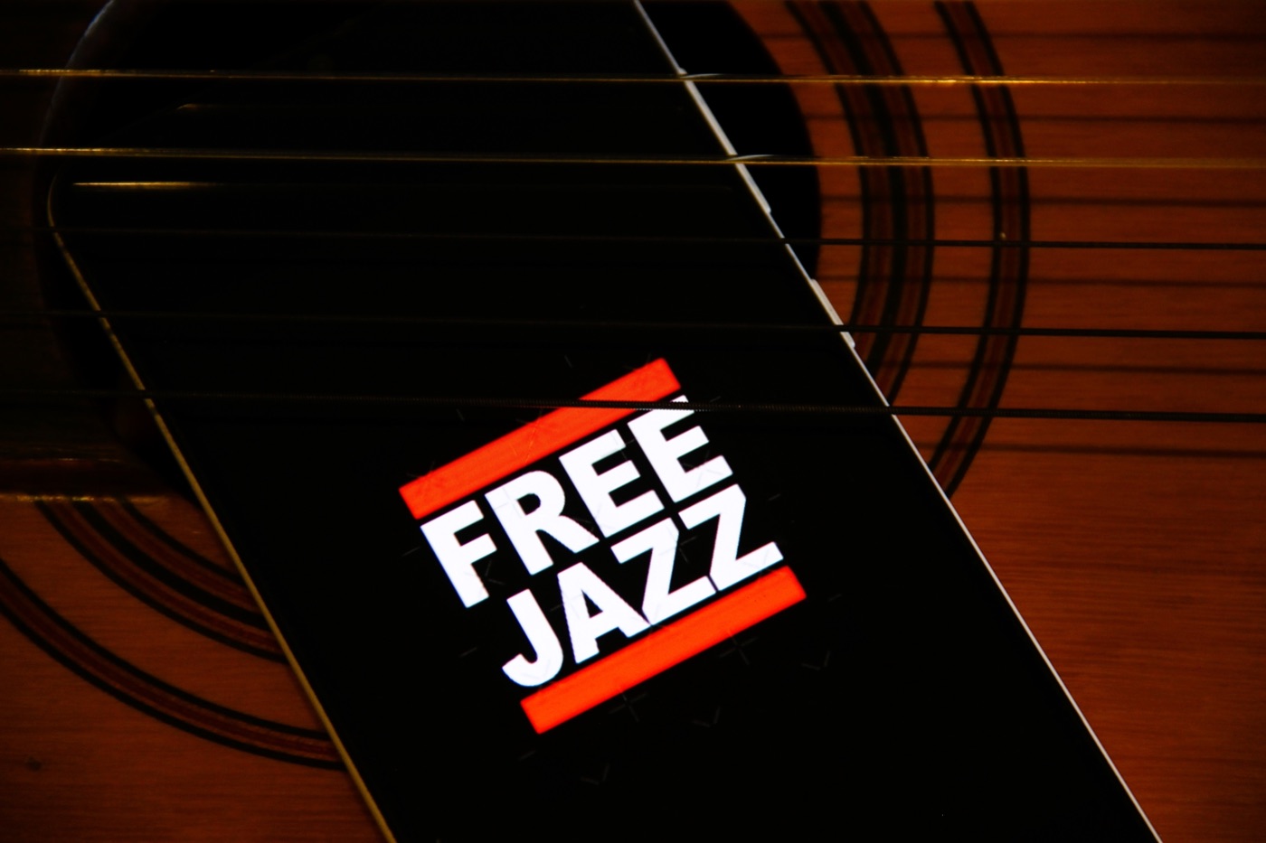 A phone showing a Free Jazz logo, resting on the strings of an acoustic guitar